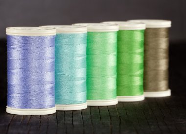 Colorful spools of thread on dark background clipart