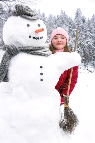 Snowman and a young girl outside in snowfall — Stock Photo, Image