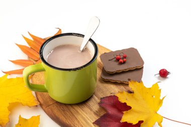 Beyaz arka planda bir fincan sıcak sıcak kahve ya da kakao. Sonbahar yaprakları ve kurabiyelerle süslenmiş.