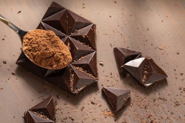 Masanın üzerinde siyah çikolata parçalanmış. Bir kaşık kakao tozu.