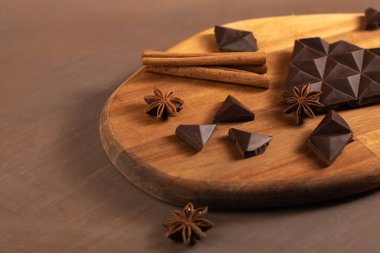 Kara acı çikolata parçalara ayrılır. Tarçın çubuklarıyla süslenmiş. Kahverengi arka plan. Düz Yatay