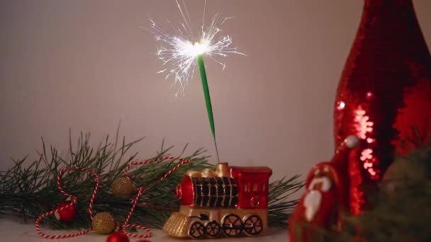 Vidéo horizontale. Une lumière brûlante du Bengale sur fond de jouets de sapin de Noël et une branche d'épinette. — Video