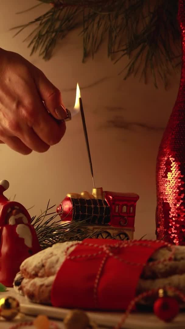 A womans hand lights a sparkler on the Christmas table. Christmas tree toys, sweet stollen pastries, — Stockvideo