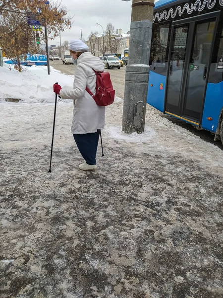 2022年1月26日，俄罗斯，莫斯科。一位孤独的老妇人手里拿着手杖走着，走到一个公交车站. 图库照片