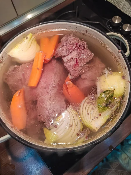 Grandi pezzi di carne vengono bolliti con cipolle e carote in una grande casseruola per la zuppa di carne. Vista dall'alto Foto Stock