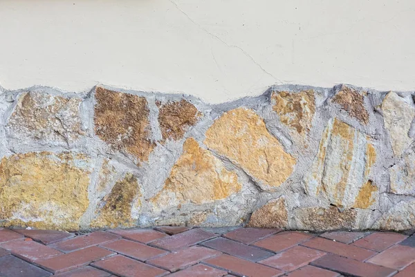Bakgrunden till en vägg med dekorativ sten och ett intilliggande golv med lagda tegelstenar. — Stockfoto