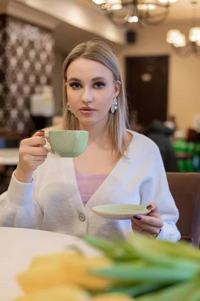 Una giovane ragazza si siede in un caffè e beve un caffè da una tazza. Modo primaverile Immagini Stock Royalty Free
