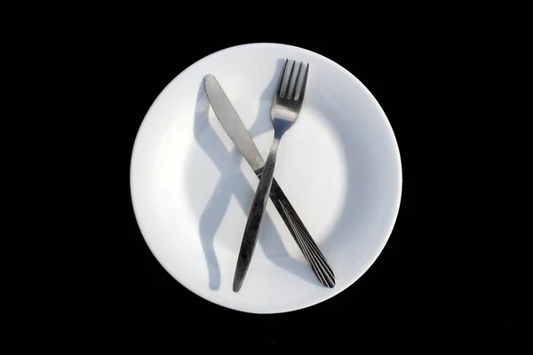 白いプレートの上に黒い背景に十字の形のナイフでフォークがあります — ストック写真