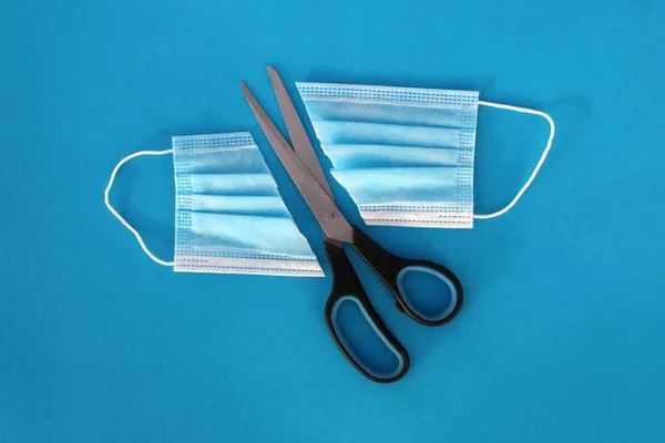 Tıbbi maske mavi arka planda makasla ikiye bölünmüş..