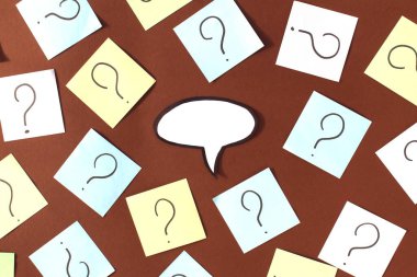 Kahverengi arka planda soru işaretleri olan kağıtlar var ve ortada düşünceler için boş bir bulut var..