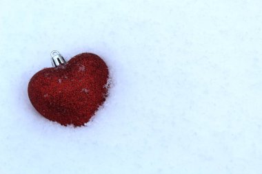Kalp şeklinde bir Noel ağacı oyuncağı karda yatıyor..