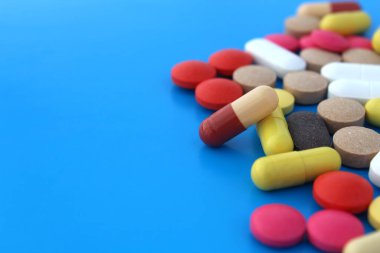 Farklı boyut ve renklerde bir yığın ilaç mavi bir arka planda yatıyor..