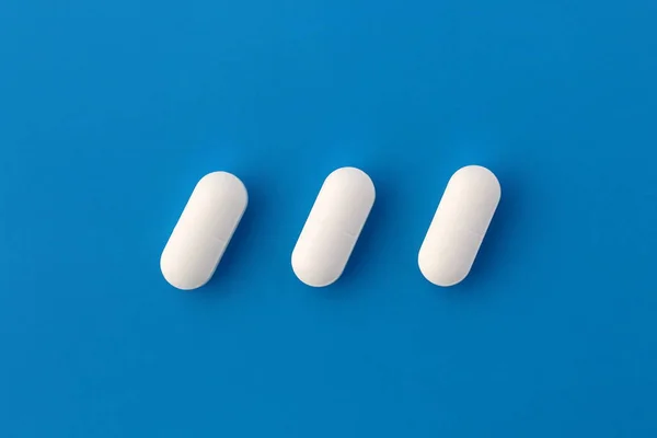 Três Comprimidos Oblongos Brancos Jazem Sobre Fundo Azul — Fotografia de Stock