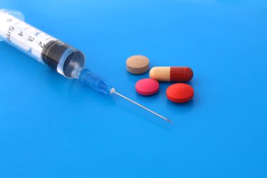 Mavi arka planda haplarla dolu bir şırınga var..