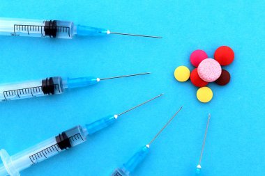 Mavi arka planda bir sürü şırınga var ve yakınlarda farklı haplar var..