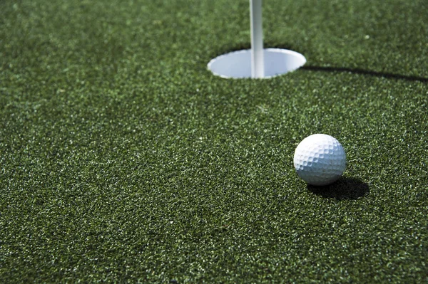 Bola de golfe e buraco em um campo — Fotografia de Stock