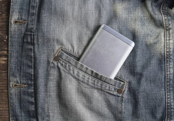Gray mobile phone in the pocket of a denim jacket