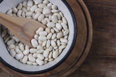 Beyaz fasulye, ahşap mutfak masasında alüminyum beyaz bir tabakta yakın plan.