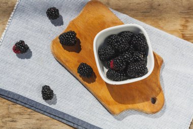 Blackberry berries close-up in a white plate on a wooden table
