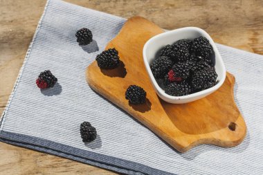 Blackberry berries close-up in a white plate on a wooden table