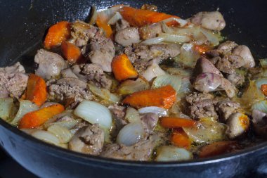Cooking fried liver with vegetables in a black frying pan, close-up