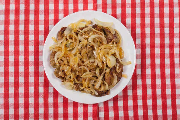 Fried liver with onions on a white round plate, top view