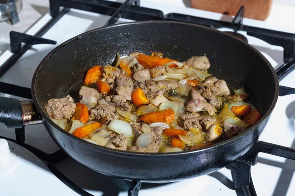 Cooking fried liver with vegetables in a black frying pan, close-up