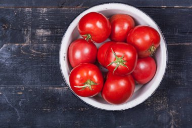 A lot of red tomatoes in an iron white plate on a black wooden table close-up