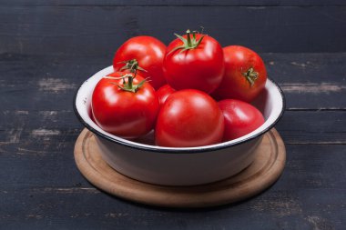 A lot of red tomatoes in an iron white plate on a black wooden table close-up