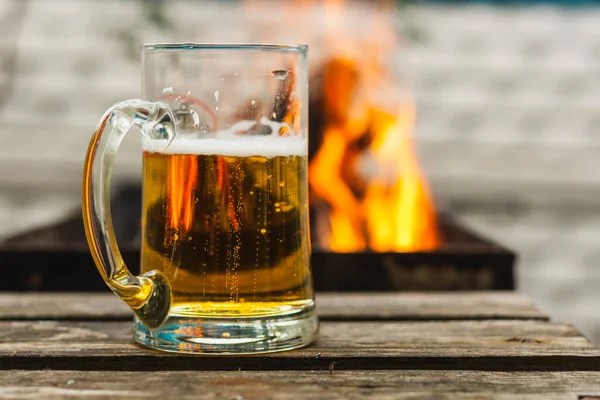 火を背景にした軽ビールのグラス ビールの大規模なガラスのクローズアップ — ストック写真