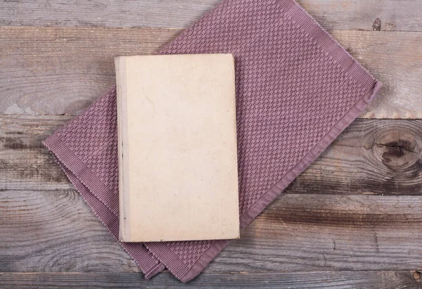 An old book with a faded cover and kitchen towels on a wooden table. Close-up of a vintage cookbook