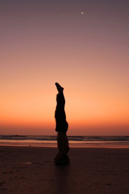 A man silhouette in a yoga pose on a sunset seashore background. clipart