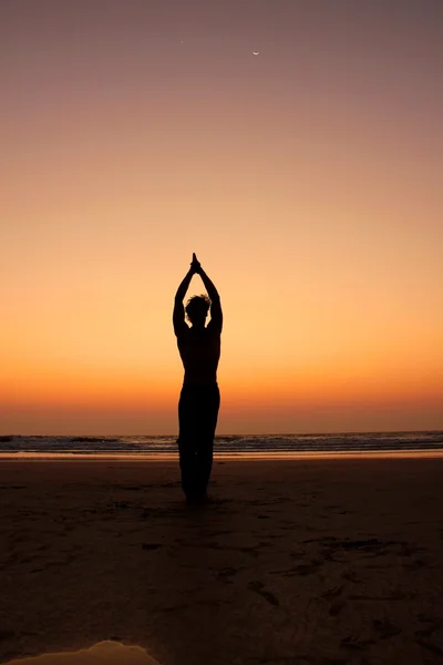 Het silhouet van een man in een yoga pose op de achtergrond van een zonsondergang kust. krijger onder de maan Stockfoto