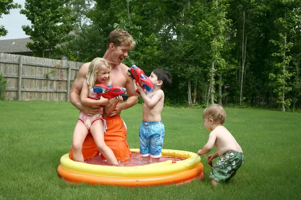 Meninos e menina brincam com o pai na piscina infantil — Fotografia de Stock