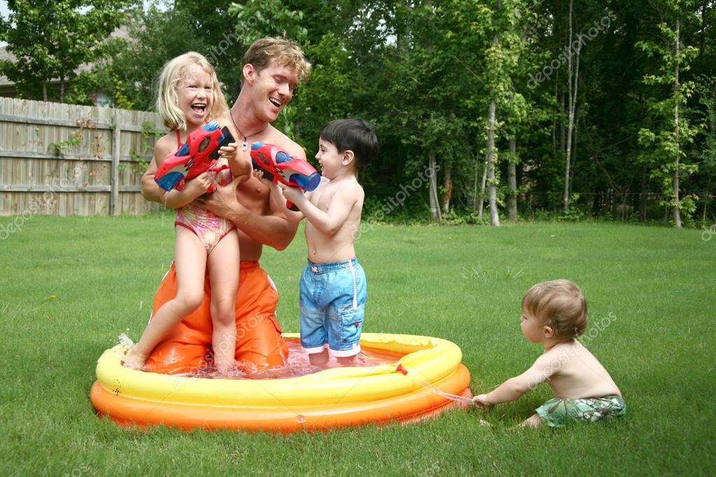 Boys and girl play with dad in the kiddie pool with water guns Stock