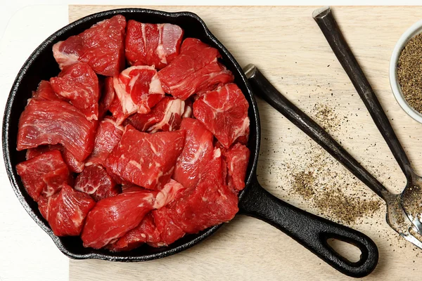 Ruwe in blokjes gesneden rundvlees in gietijzer koekepan op tafel — Stockfoto