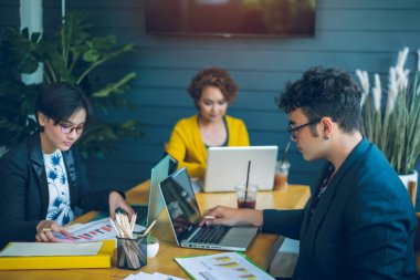 Ofis masasında bir grup meslektaşlarıyla oturan kendine güvenen genç işadamları işlerini analiz etmek ve planlamak için dizüstü bilgisayar ve grafik çizelgeleri kullanarak çalışırlar..
