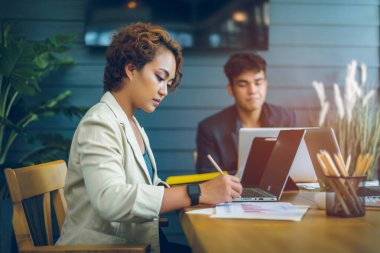 Asyalı sarışın iş kadını iş performansını ve şirket gelişimini gösteren grafikleri analiz ediyor. O ve meslektaşları dizüstü bilgisayarlar üzerinde çalışıyorlar. Kopya alanlarıyla ilgili büyük niyetleri var..