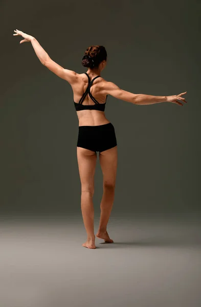 身穿黑色泳衣的漂亮女子芭蕾舞舞蹈演员在浅灰工作室的背景下表演。动物本能 — 图库照片