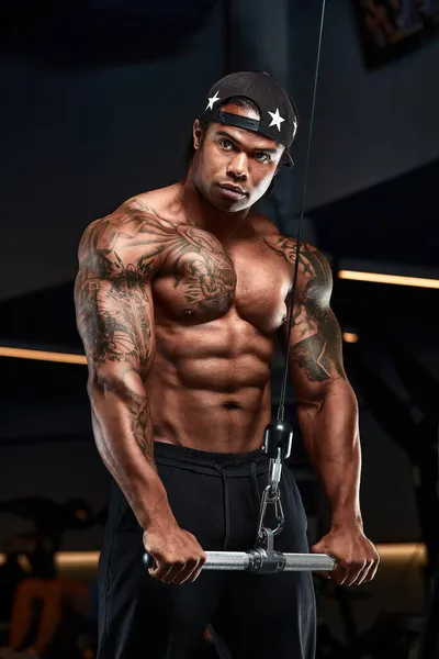 Güçlü ve kaslı esmer tenli adam spor salonunda modern ekipmanlarla antrenman yapıyor. Kaslı şişirilmiş fitness eğitmeninin portresi — Stok fotoğraf