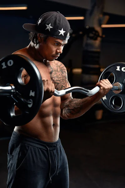 Ein kräftiger und muskulöser Mann mit dunkler Hautfarbe trainiert an modernen Geräten im Fitnessstudio. Porträt eines muskelbepackten Fitnesstrainers — Stockfoto