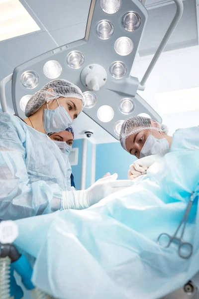 Equipo quirúrgico concentrado operando a un paciente en un quirófano. Anestesiólogo bien entrenado con años de entrenamiento con máquinas complejas sigue al paciente durante toda la cirugía — Foto de Stock