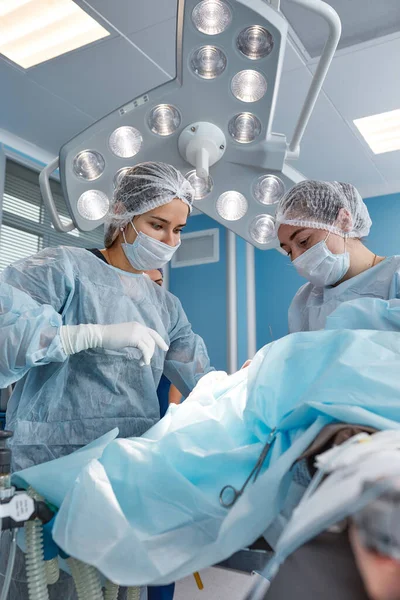 Konsantre cerrahi ekibi ameliyathanede bir hastayı ameliyat ediyor. Karmaşık makinelerle yıllarca eğitim almış iyi eğitimli bir anestezi uzmanı ameliyat boyunca hastayı takip eder. — Stok fotoğraf