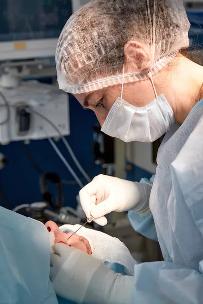 Kan pıhtılaşması geçiren bir hastanın yüzünü kapatın. Cerrah göz kapağını keser ve tıbbi aletlerle manipülasyon yapar. — Stok fotoğraf