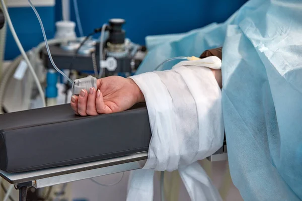 Το χέρι των ασθενών είναι κάτω από τον ορό με ένα παλμικό οξύμετρο στο δάχτυλο. Ιατρικές υπηρεσίες. — Φωτογραφία Αρχείου