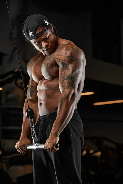 Güçlü ve kaslı esmer tenli adam spor salonunda modern ekipmanlarla antrenman yapıyor. Kaslı şişirilmiş fitness eğitmeninin portresi — Stok fotoğraf