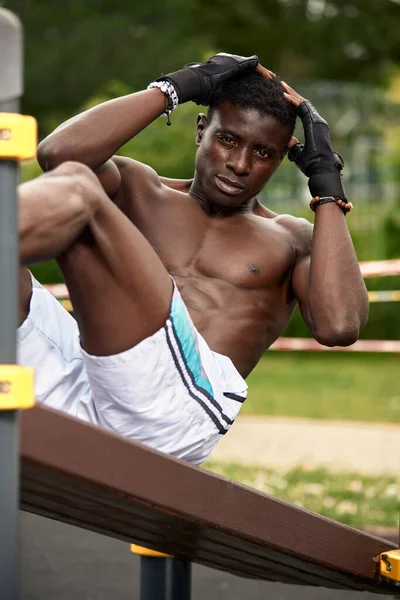 Retrato de un atleta negro que se extiende en un parque. Está usando ropa negra activa. — Foto de Stock