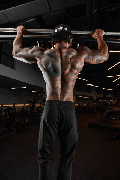 Ein kräftiger und muskulöser Mann mit dunkler Hautfarbe trainiert an modernen Geräten im Fitnessstudio. Porträt eines muskelbepackten Fitnesstrainers — Stockfoto
