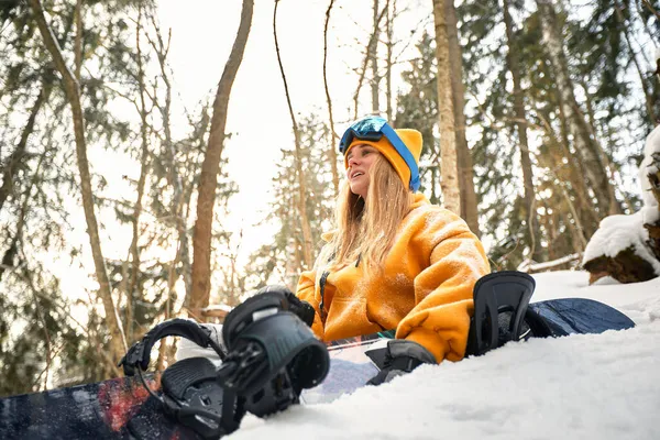 Mujer caucásica snowboarder sostiene snowboard sobre hermoso fondo de bosque nevado en día soleado. —  Fotos de Stock