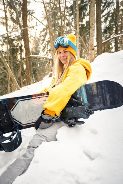 Mulher branca snowboarder detém snowboard no belo fundo da floresta nevada em dia ensolarado. — Fotografia de Stock